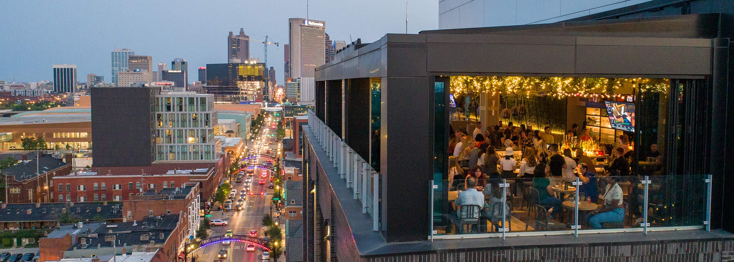 Drone view of Lincoln Social rooftop lounge with guests, facing Downtown Columbus showing High Street traffic below