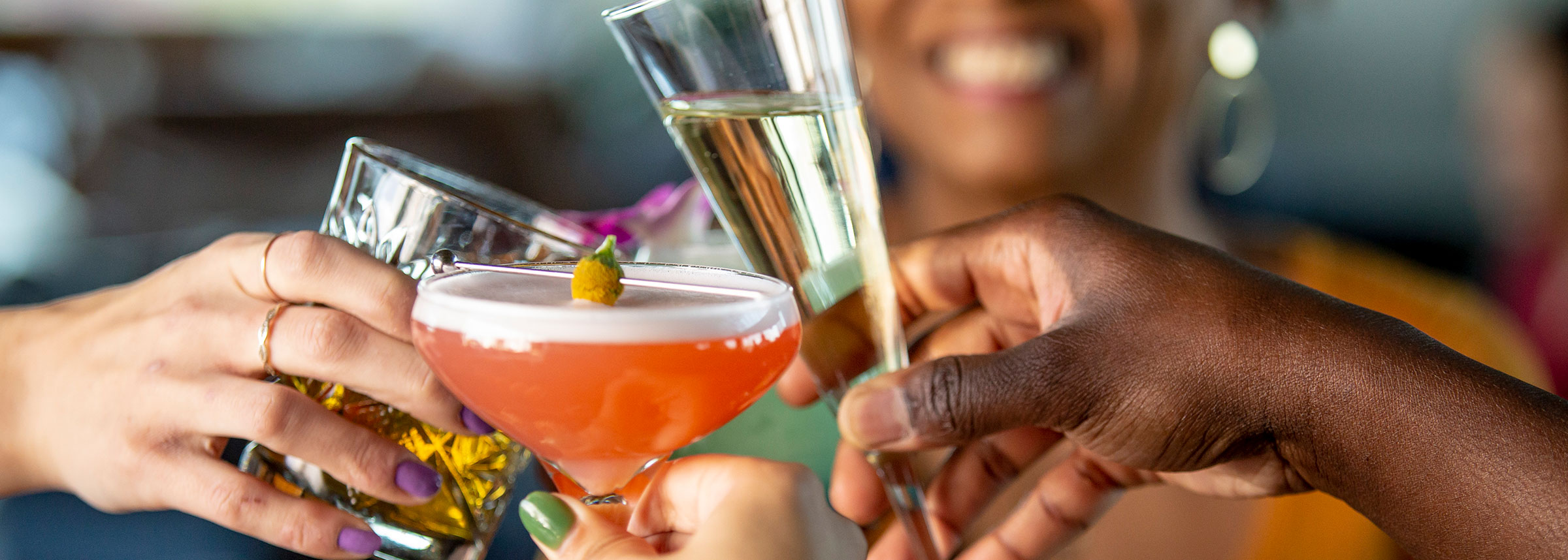 Three hands holding cocktails and champagne clinking glasses in toast